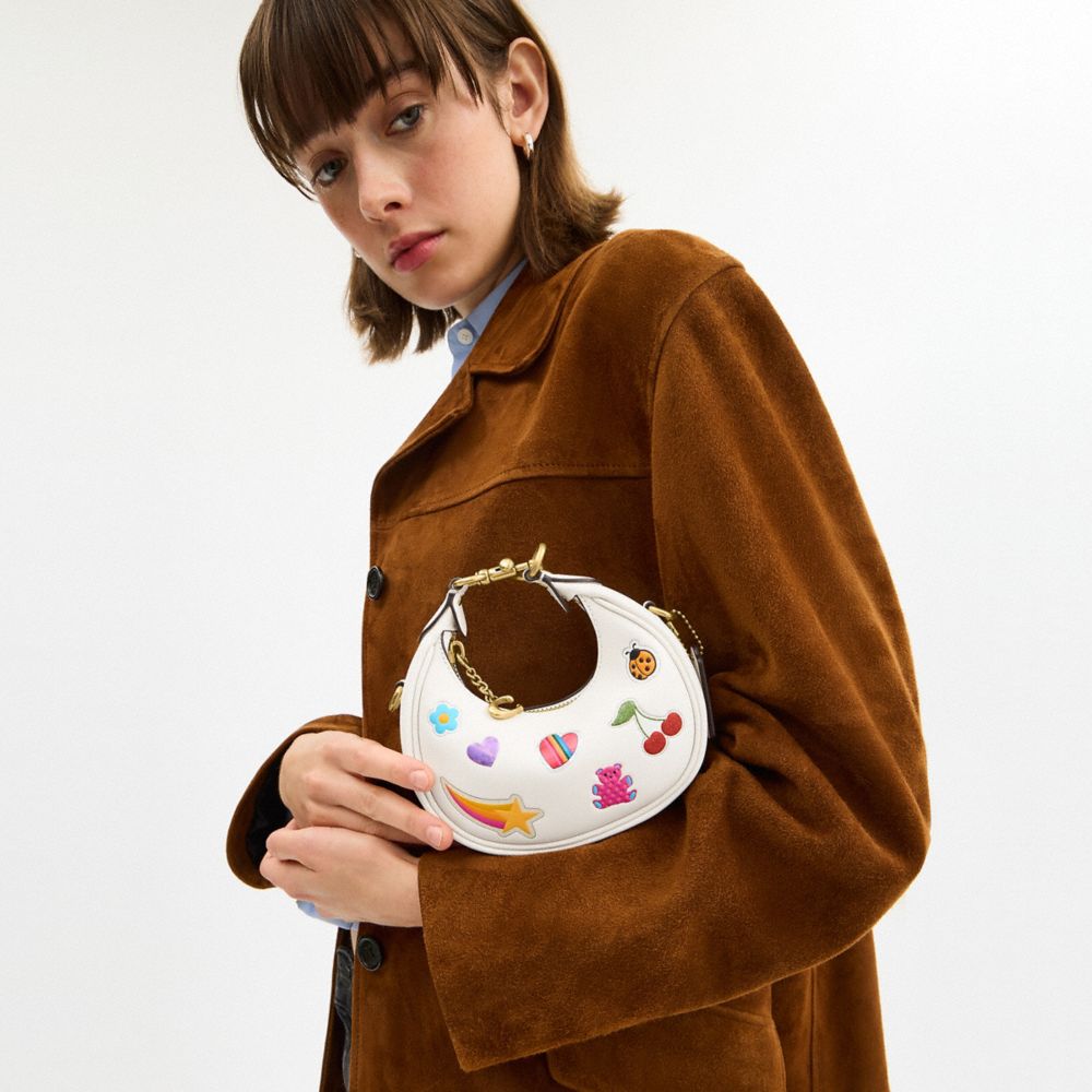 COACH®,Jonie Bag With Sticker Print,Leather,Fabric,Crossbody,Logo,Pendant,Circle,Embellished,Stitching,Piping,Pattern,Grap...,White,Detail View